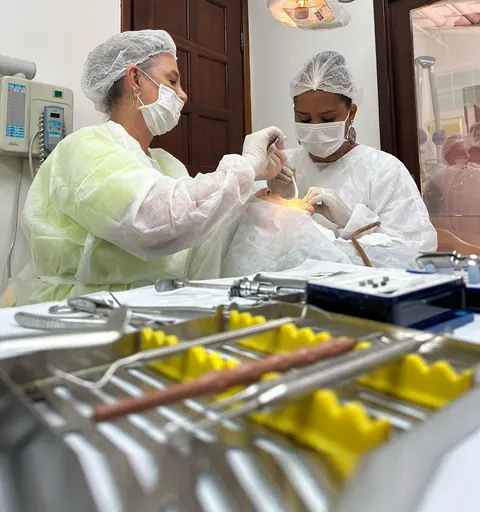 Dra. Zeli de touca e máscara atendendo uma paciente no consultório odontológico.