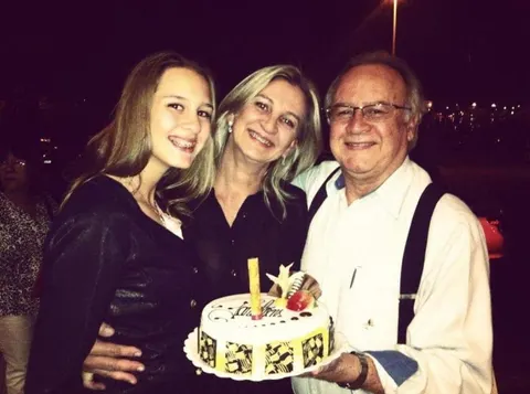 Zeli entre a filha e o marido Adjacy, que segura um bolo de aniversário, em uma noite de festa.