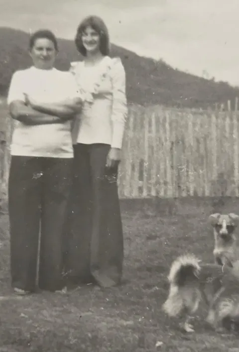 Fotografia antiga em preto e branco: Zeli jovem ao lado de outra mulher, em um campo, com um cachorro.