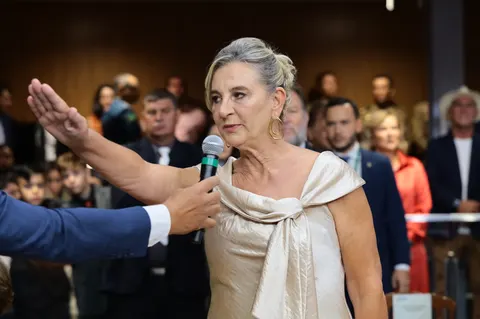 Dra. Zeli fala ao microfone, com a mão erguida, durante cerimônia na Assembleia.