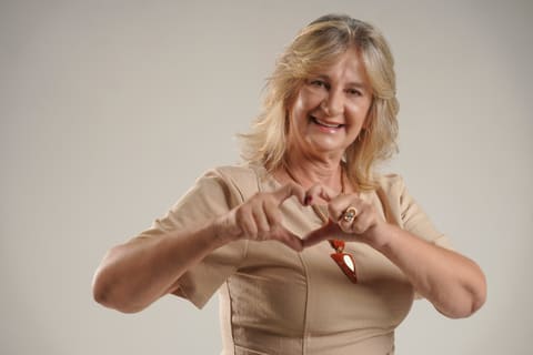 Dra. Zeli faz um coração com as mãos, sorrindo, em retrato de estúdio.